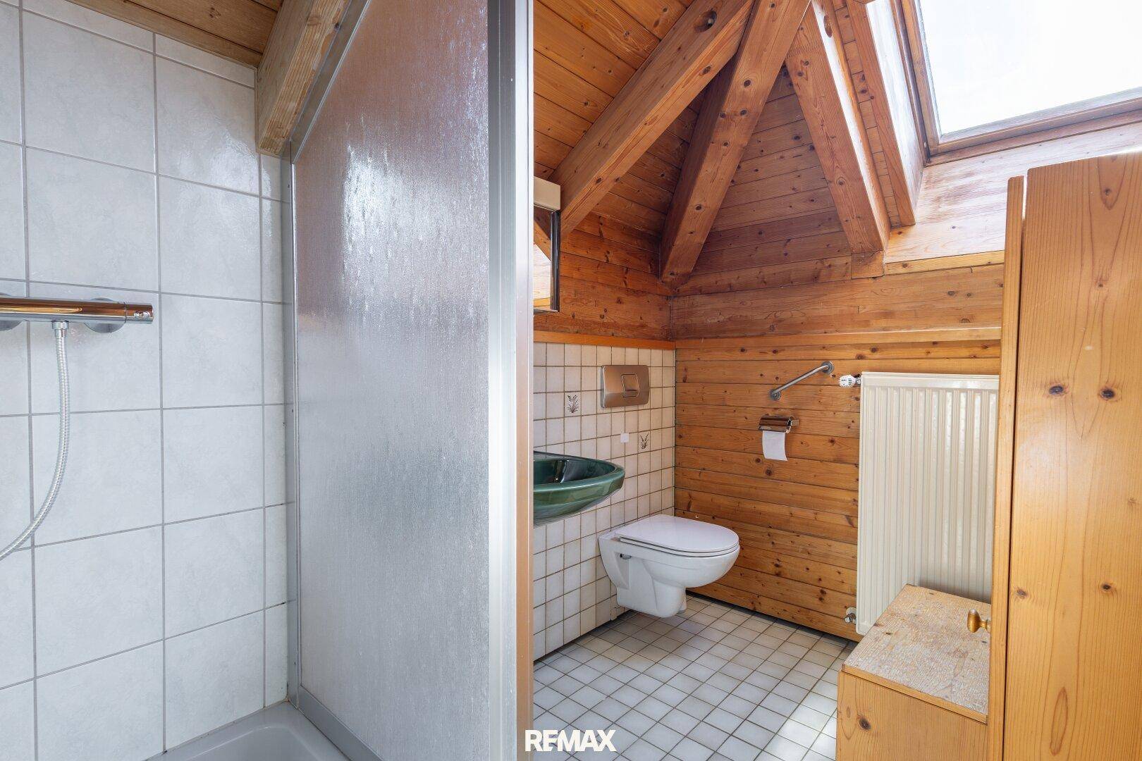Badezimmer im Dachgeschoss mit Dusche, Holzwänden und Dachfenster.