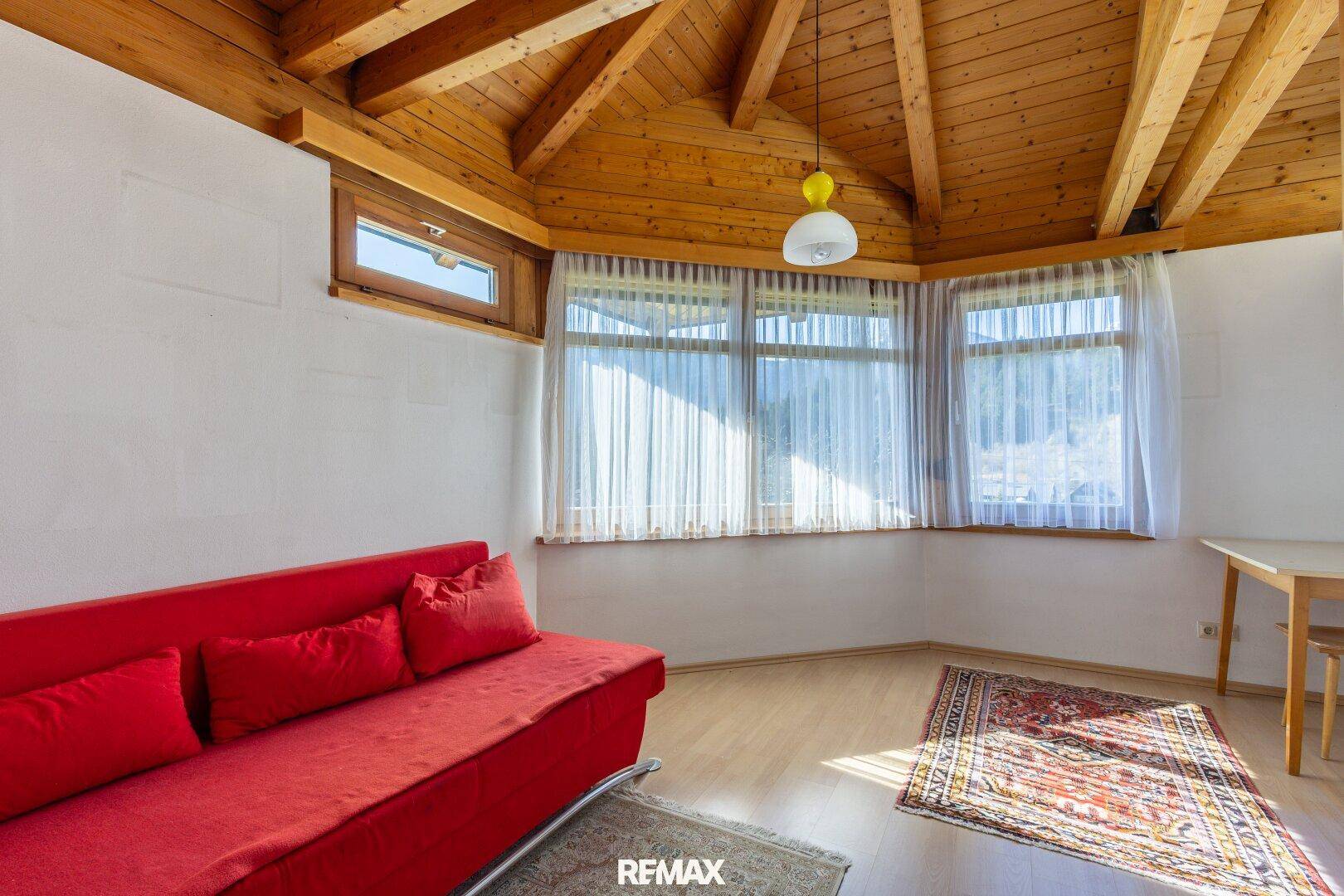 Helles Schlafzimmer mit Holzdachschrägen, rotem Sofa und Holzboden.