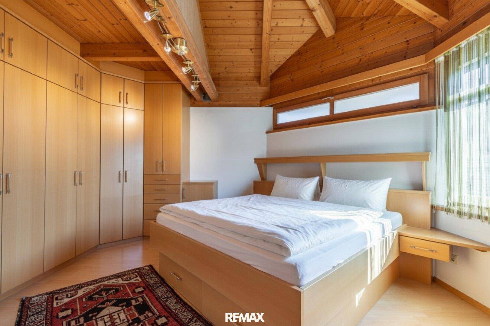Gemütliches Schlafzimmer mit Holzdachschrägen, Einbauschränken und Holzboden.