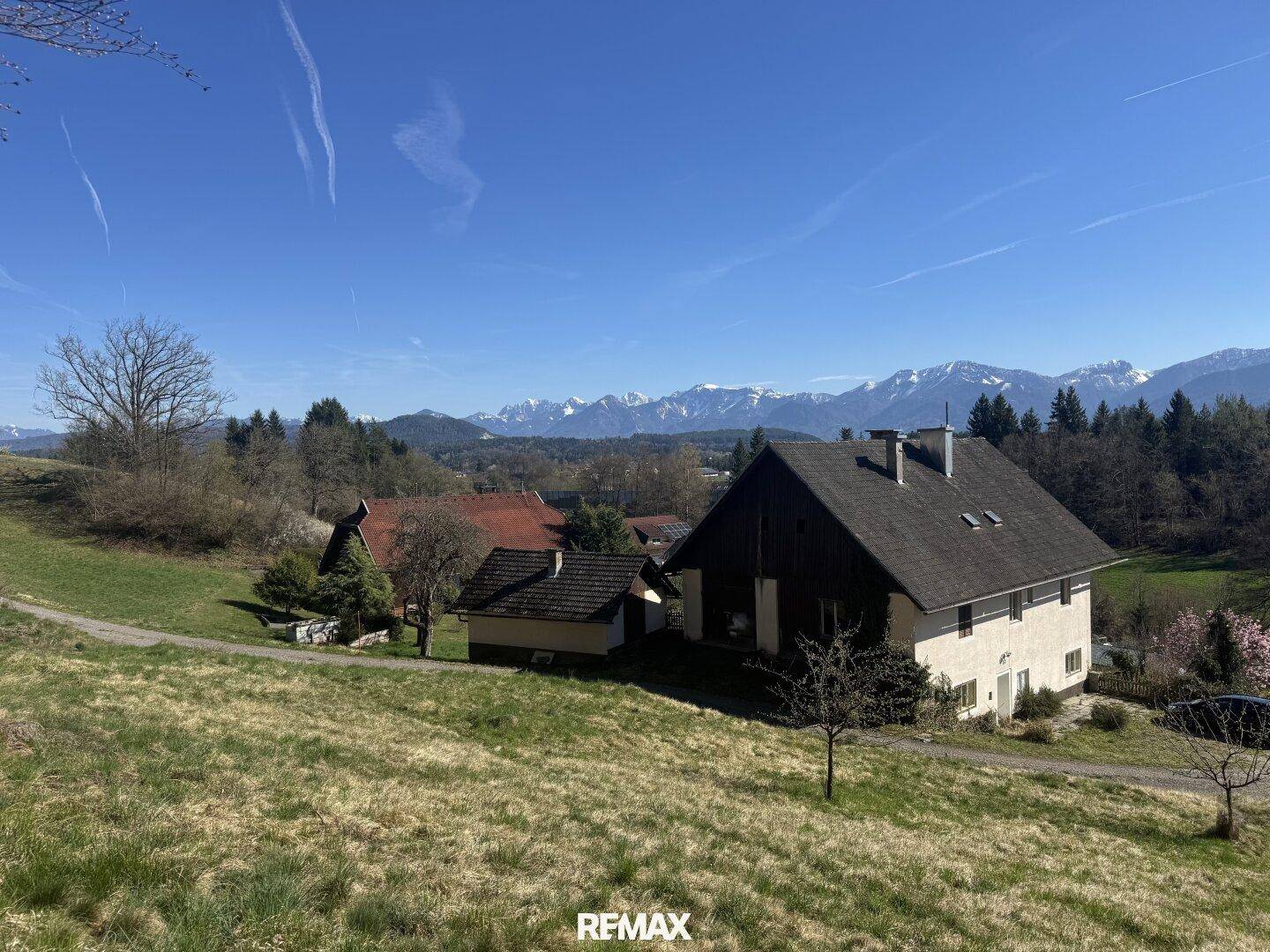 Haus in Hanglage mit weitem Blick über grüne Wiesen und die beeindruckende Bergkulisse.