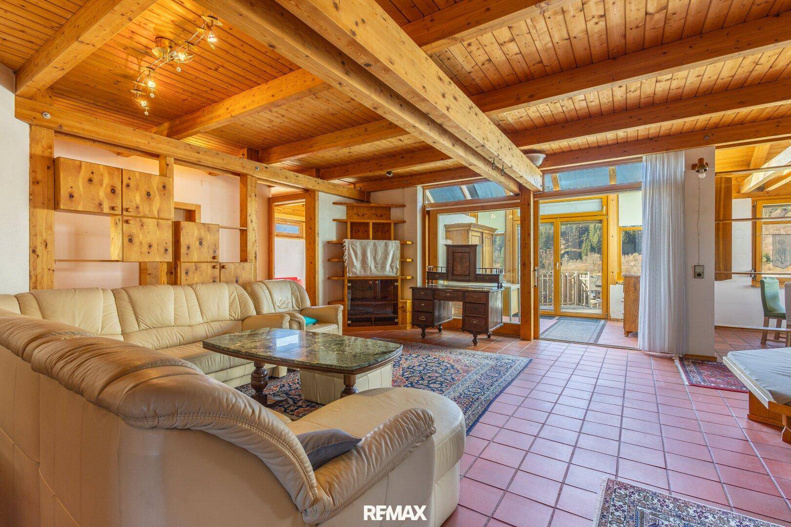 Geräumiges Wohnzimmer mit Holzbalkendecke, Terrakottafliesen und beiger Ledercouch.