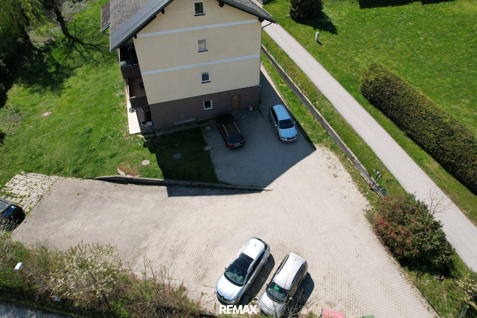 Rückansicht des Gebäudes mit Parkplätzen und angrenzender Grünfläche.