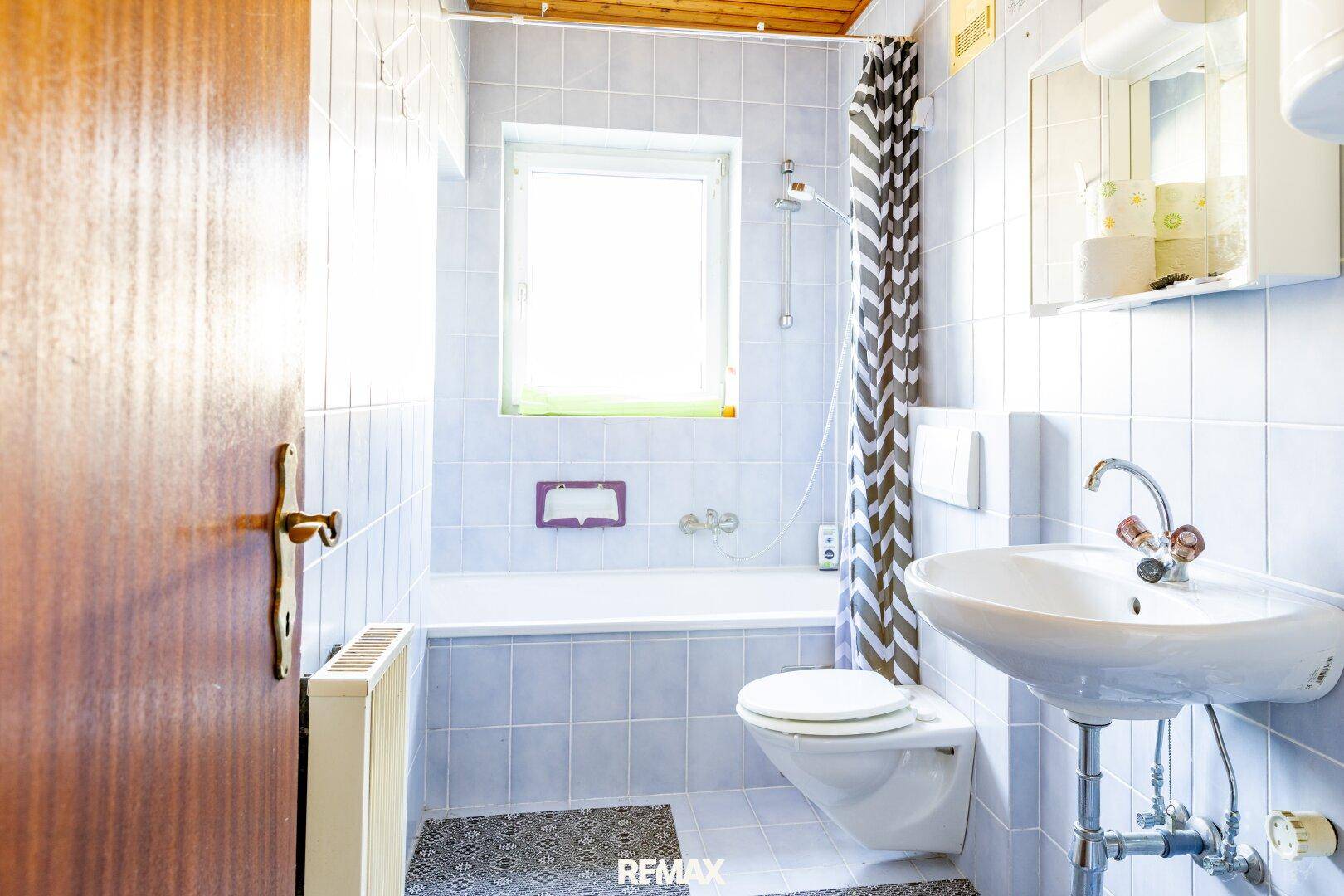 Badezimmer mit hellblauen Fliesen, Badewanne mit Duschvorhang, WC und Waschbecken.