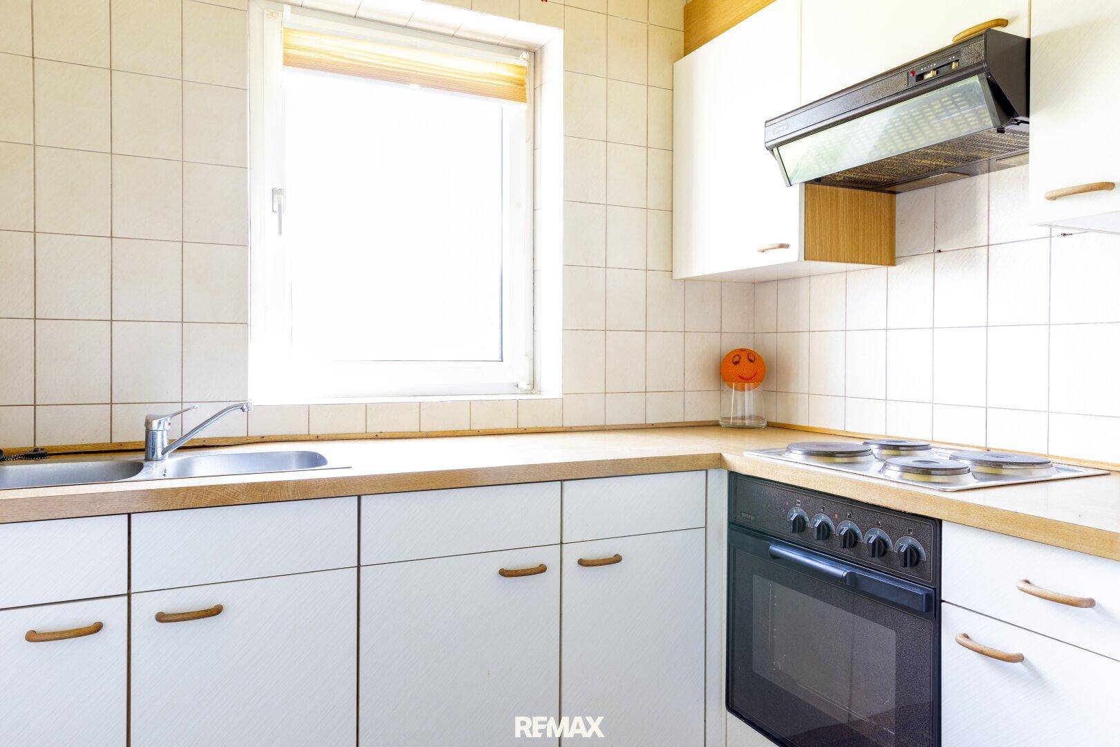 Funktionale Küche mit weißen Schränken, Holz-Arbeitsplatte und Elektroherd.