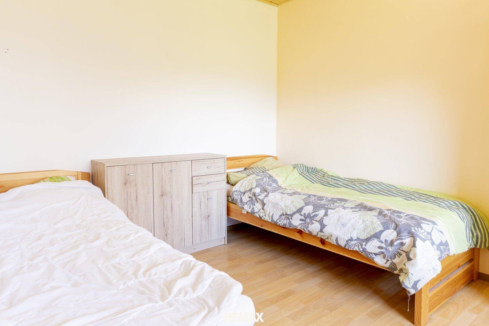 Schlafzimmer mit zwei Einzelbetten, hellem Holzboden und einfacher Einrichtung.
