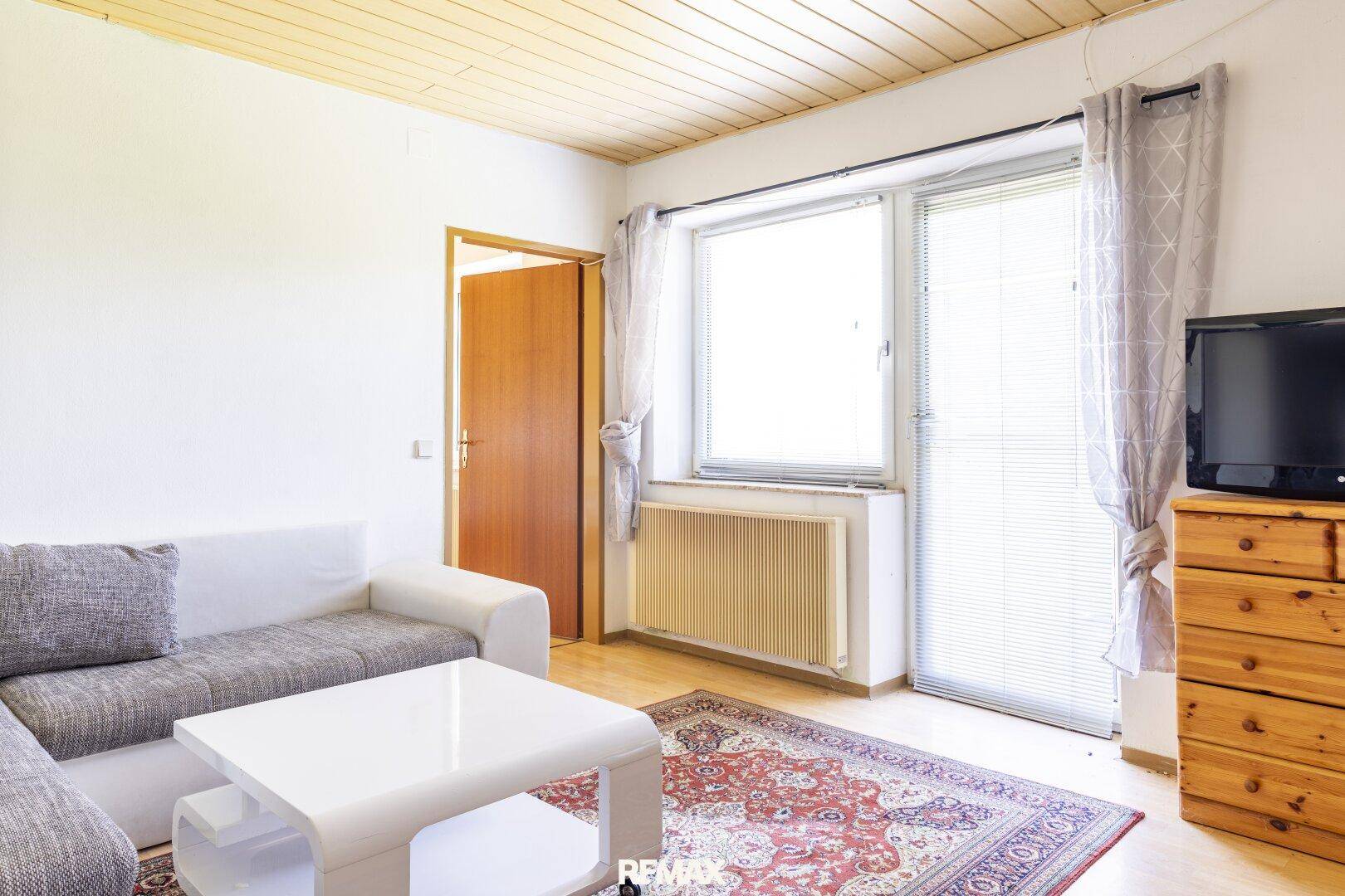 Helles Wohnzimmer mit Sofa, Couchtisch und Zugang zu einem Balkon.