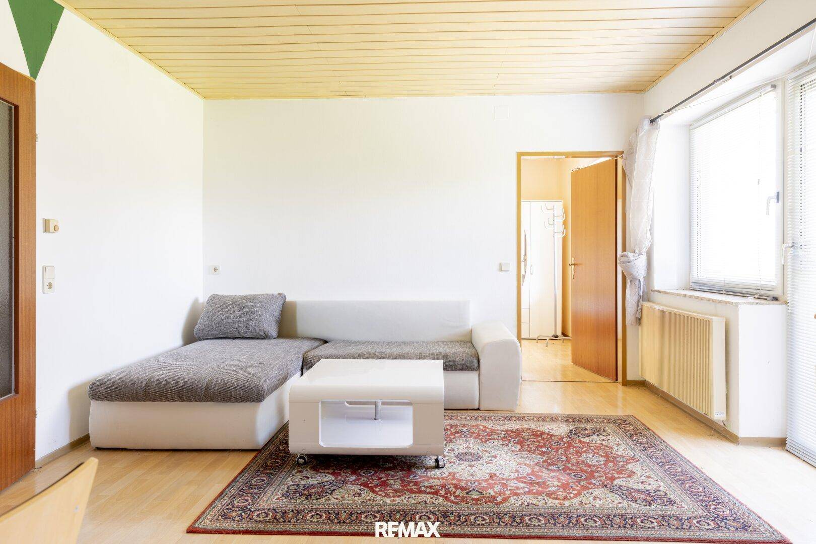 Helles Wohnzimmer mit Parkettboden, gemütlichem Sofa und Blick ins Grüne durch das Fenster.