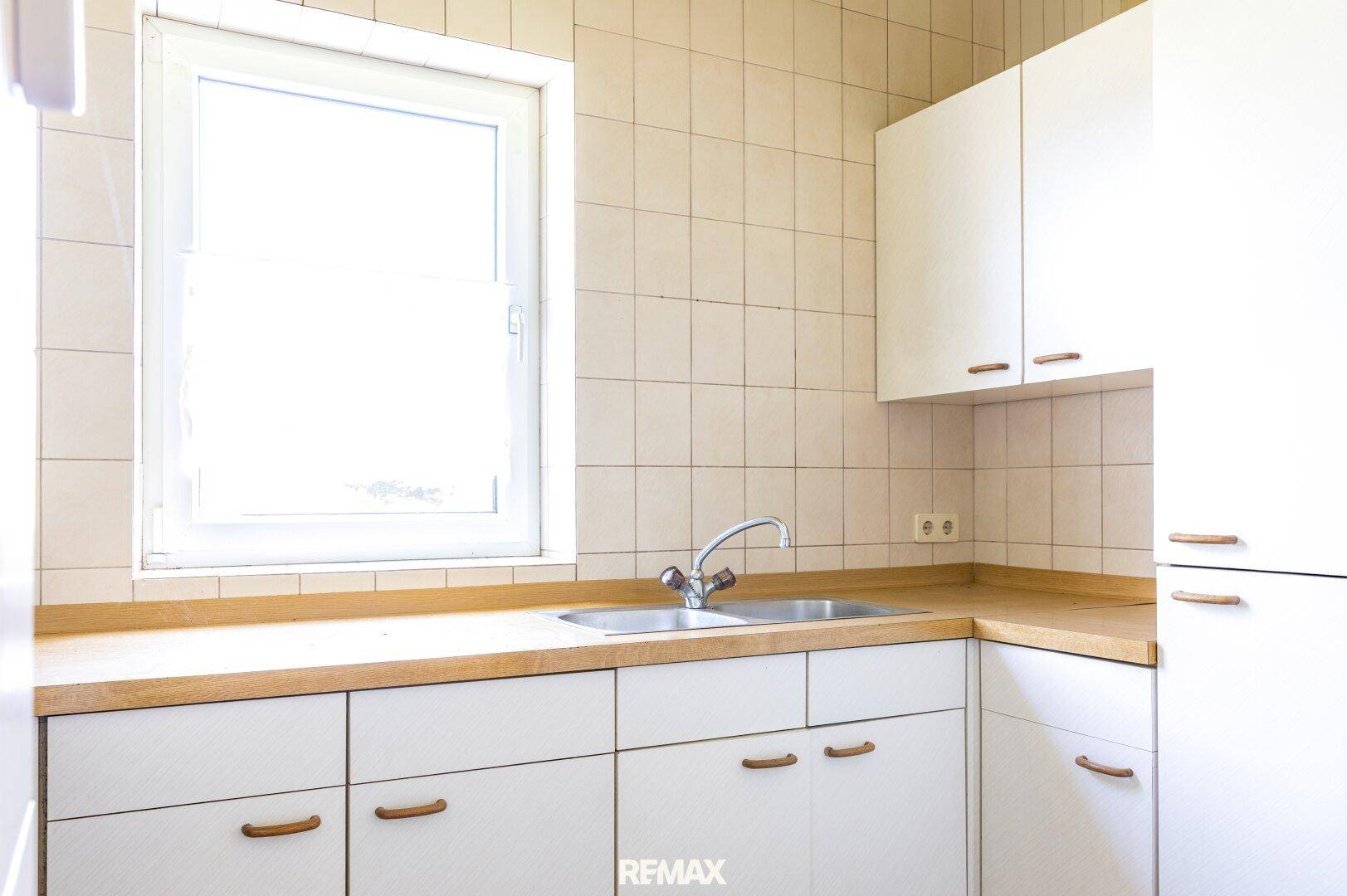 Helle Küche mit weißen Unterschränken, Holz-Arbeitsplatte und Spülbecken.