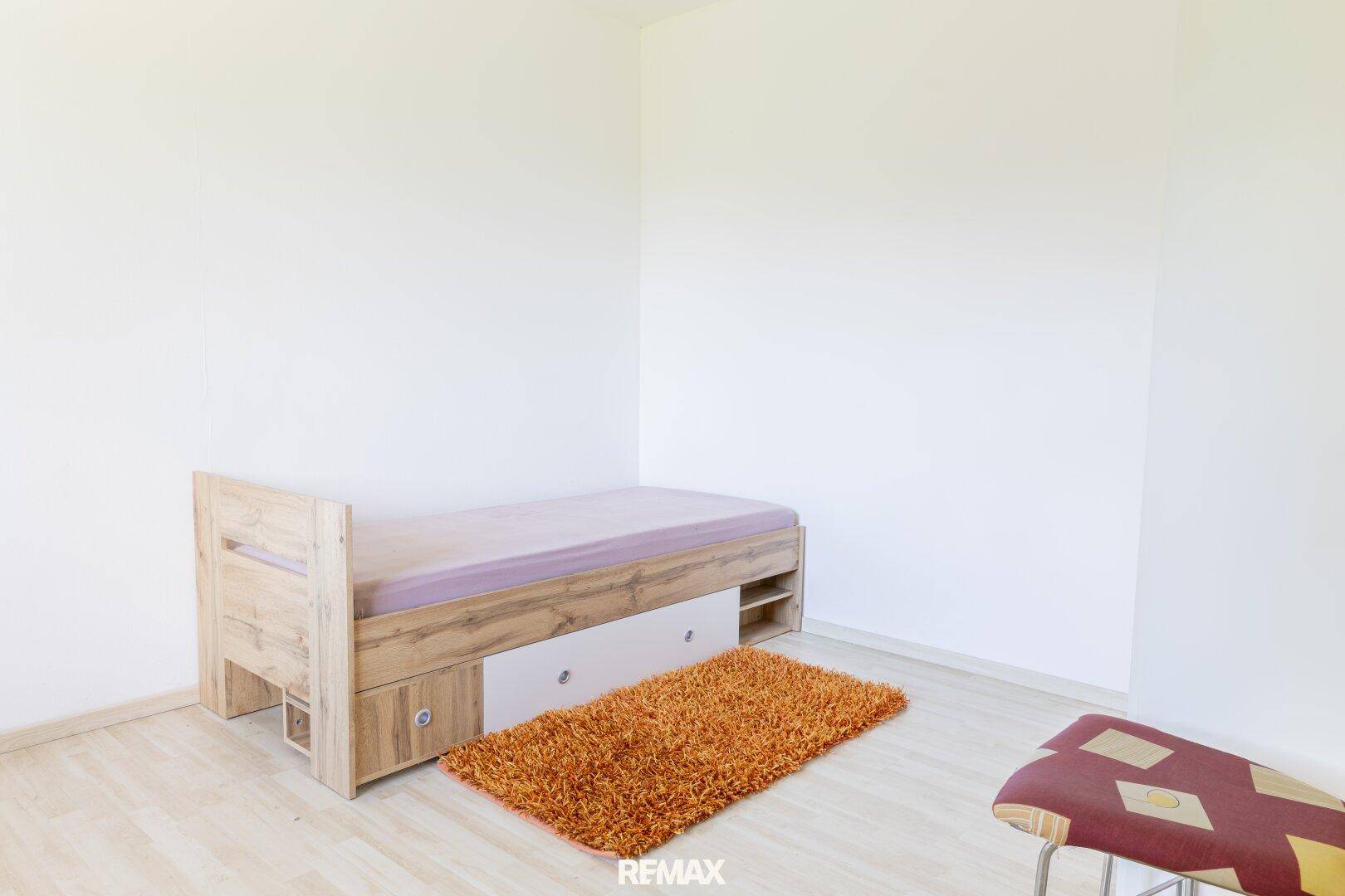 Helles Schlafzimmer mit Einzelbett, integriertem Stauraum und einem flauschigen Teppich.