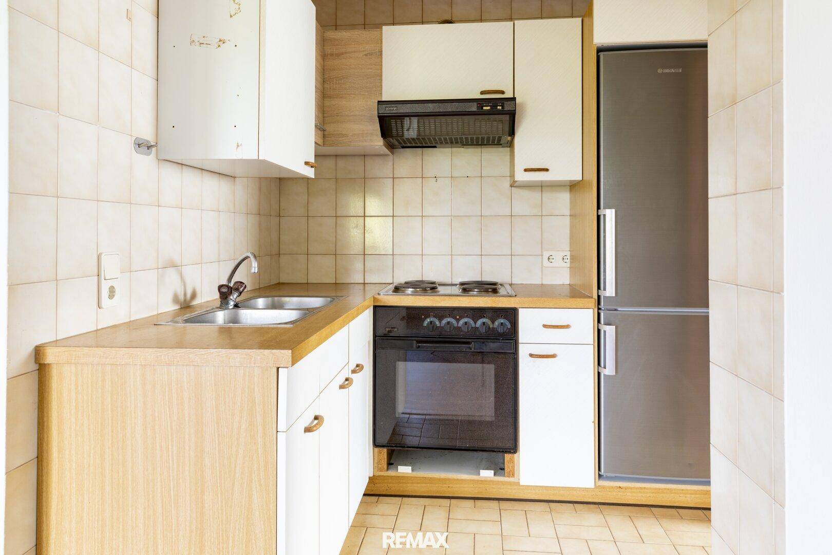 Funktionale Küche mit weißen Schränken, Holz-Arbeitsplatte, Herd, Spüle und Kühlschrank.