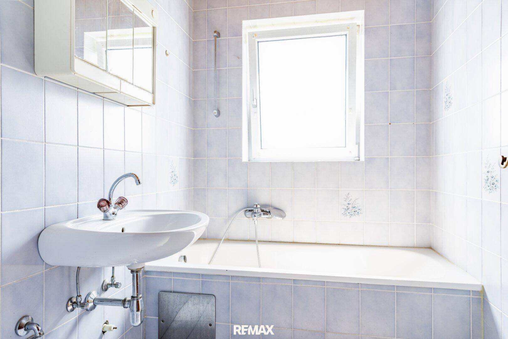 Badezimmer mit Badewanne, Waschbecken, Spiegelschrank und einem Fenster für natürliche Belüftung.
