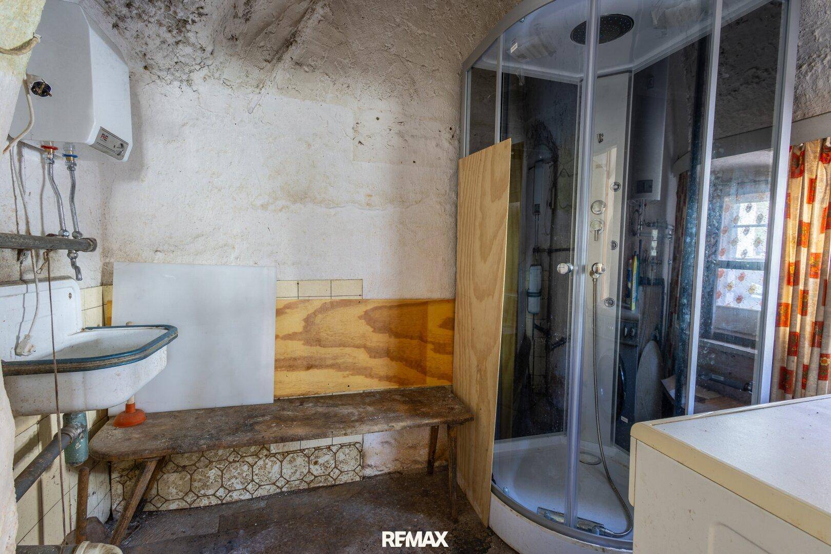 Einfaches Badezimmer mit Duschkabine, Waschbecken und älteren Fliesen.