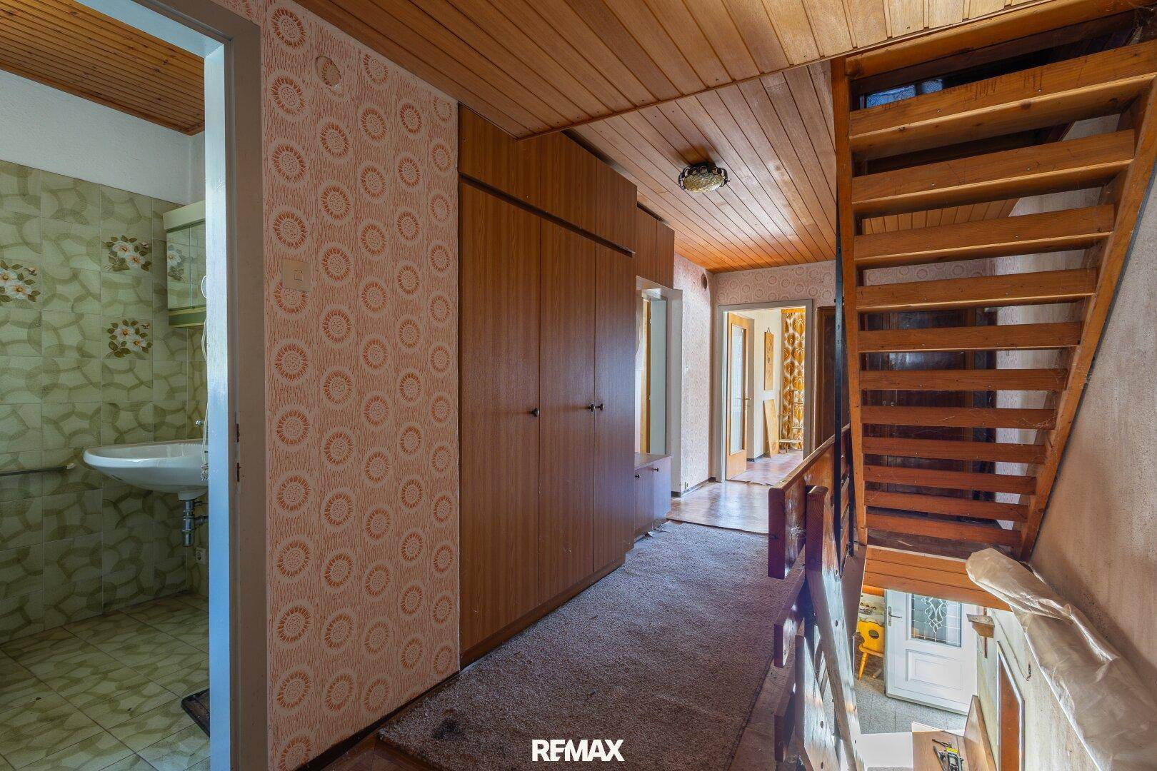 Flur mit Holztreppe, Einbauschränken und gemusterten Tapeten im Vintage-Stil.