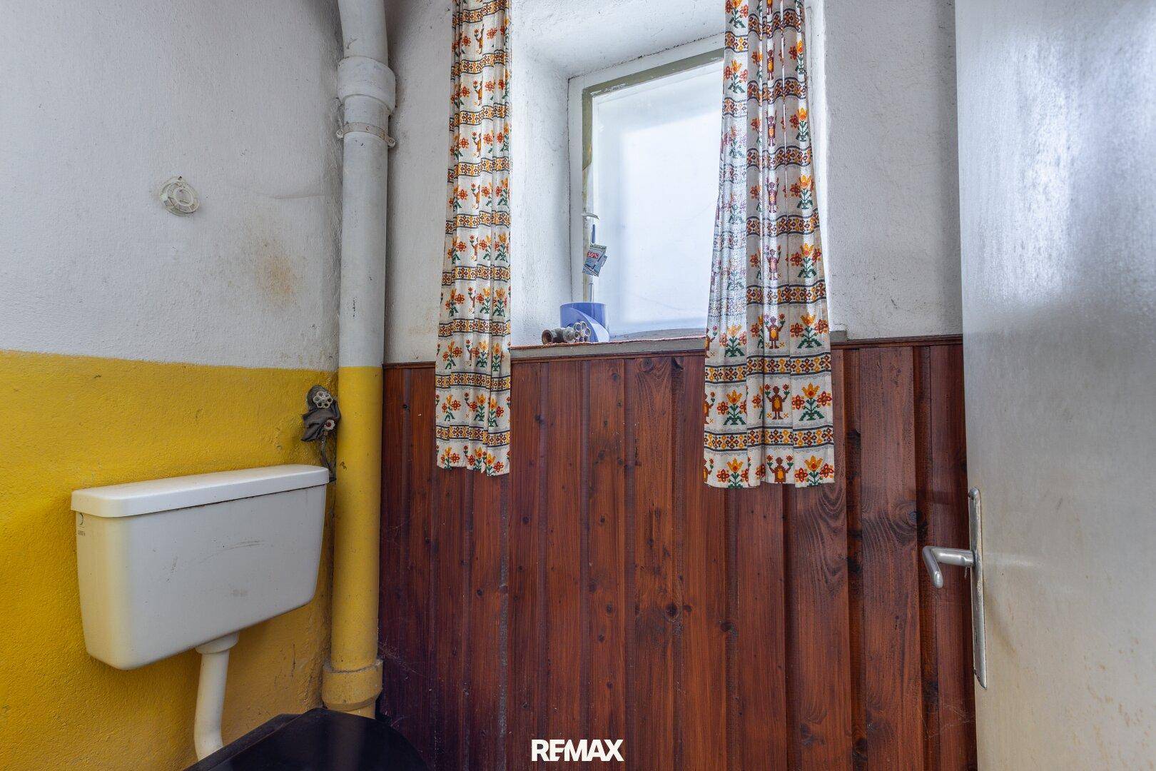 Kleine Toilette mit Fenster, Holzverkleidung und gelb gestrichenen Wänden.