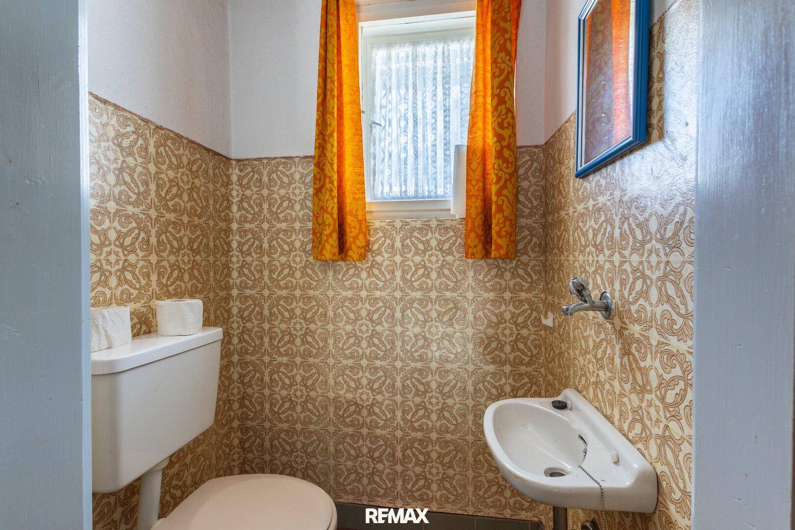 Kleine Toilette mit WC, Waschbecken und gemusterten Fliesen im Vintage-Stil.