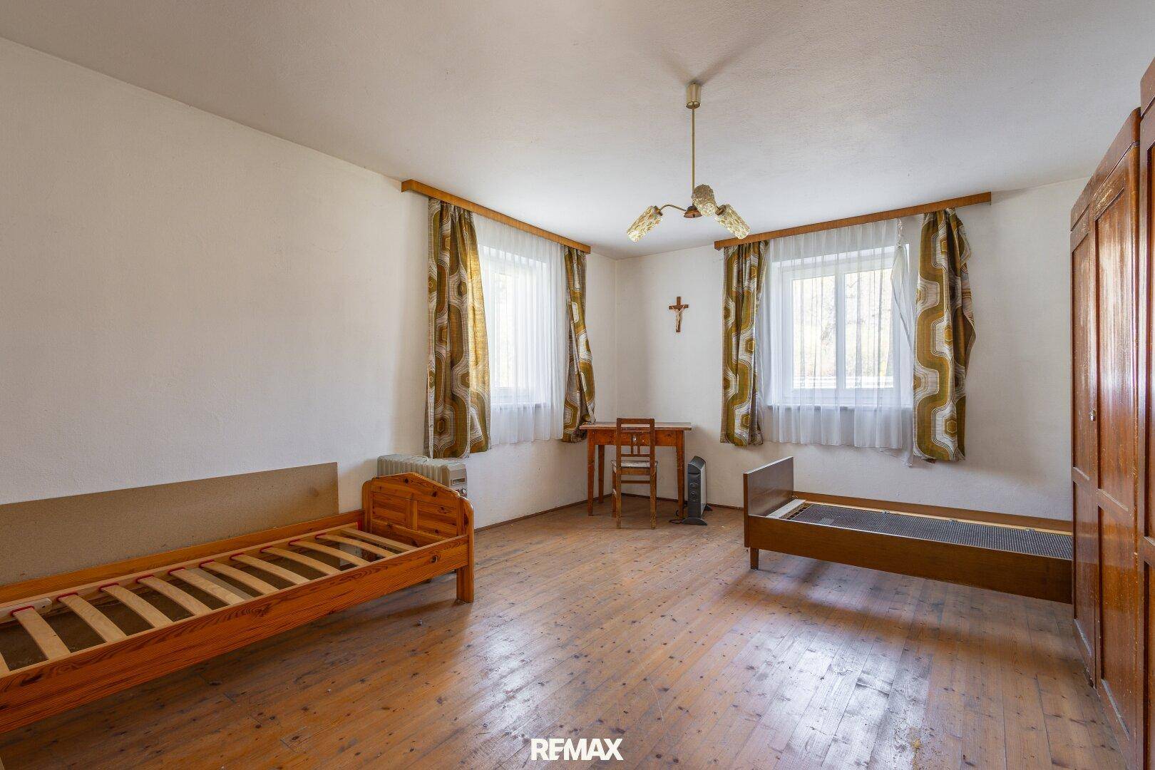 Geräumiges Schlafzimmer mit zwei Einzelbetten, Holzboden und Fenstern mit Vorhängen.