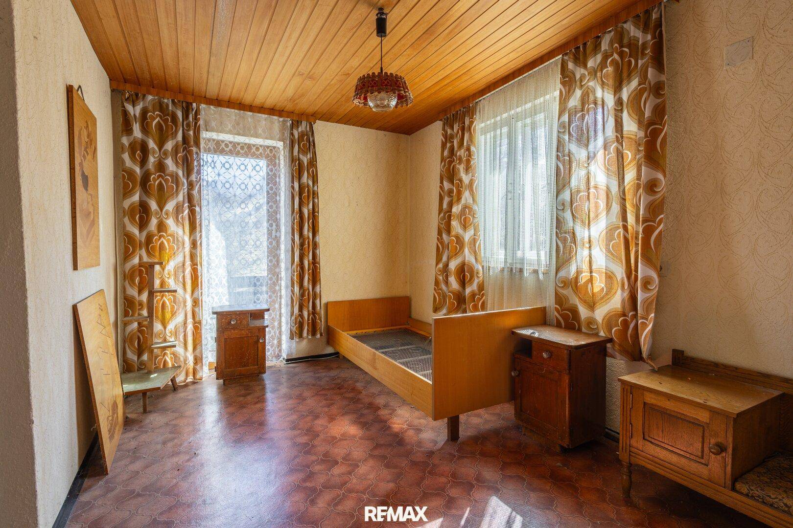Schlafzimmer mit Holzbalkendecke, Einzelbett und gemusterten Vorhängen im Retro-Stil.