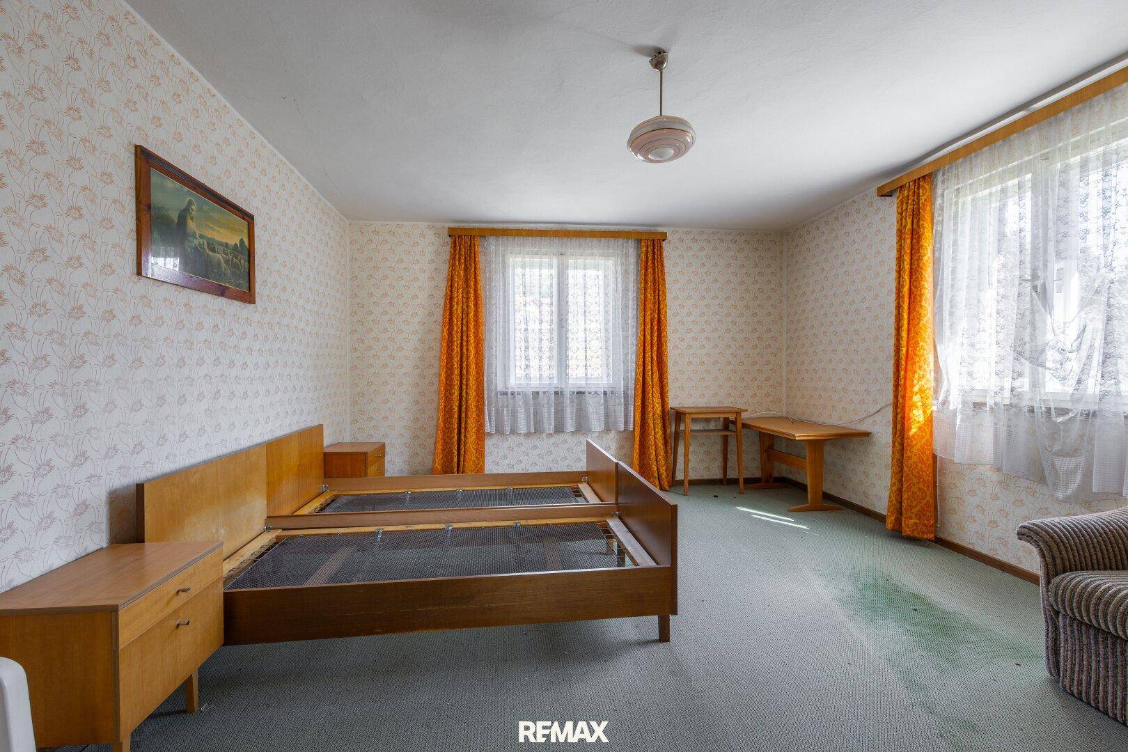 Helles Schlafzimmer mit zwei Einzelbetten, Teppichboden und orangefarbenen Vorhängen.