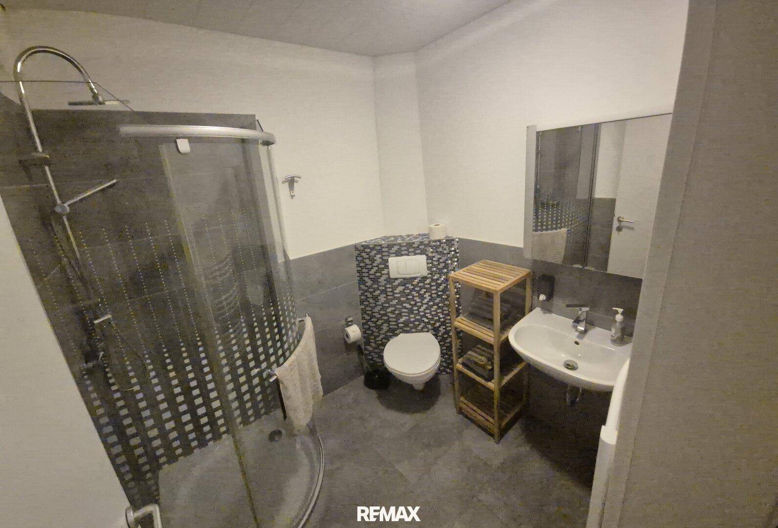 Modernes Badezimmer mit Duschkabine, Toilette und Waschbecken, in dunklen Farbtönen gehalten.
