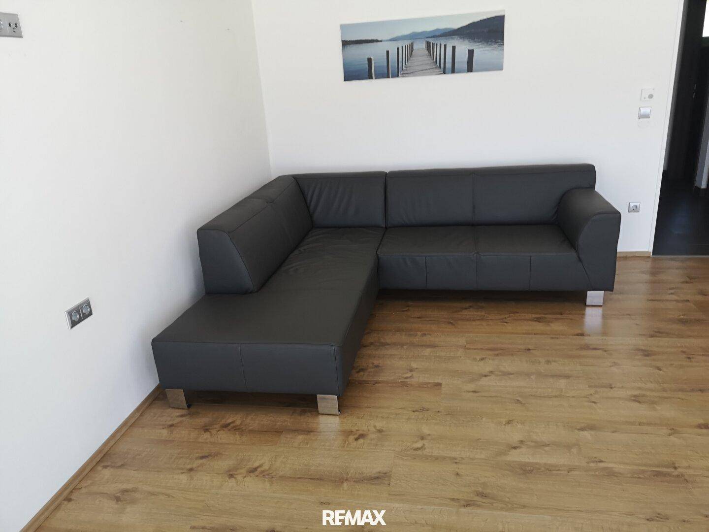 Modernes Wohnzimmer mit dunkelgrauem Ecksofa und hellem Laminatboden.