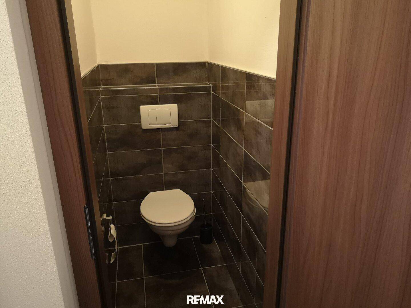 Kleines Gäste-WC mit dunklen Fliesen und wandmontierter Toilette.