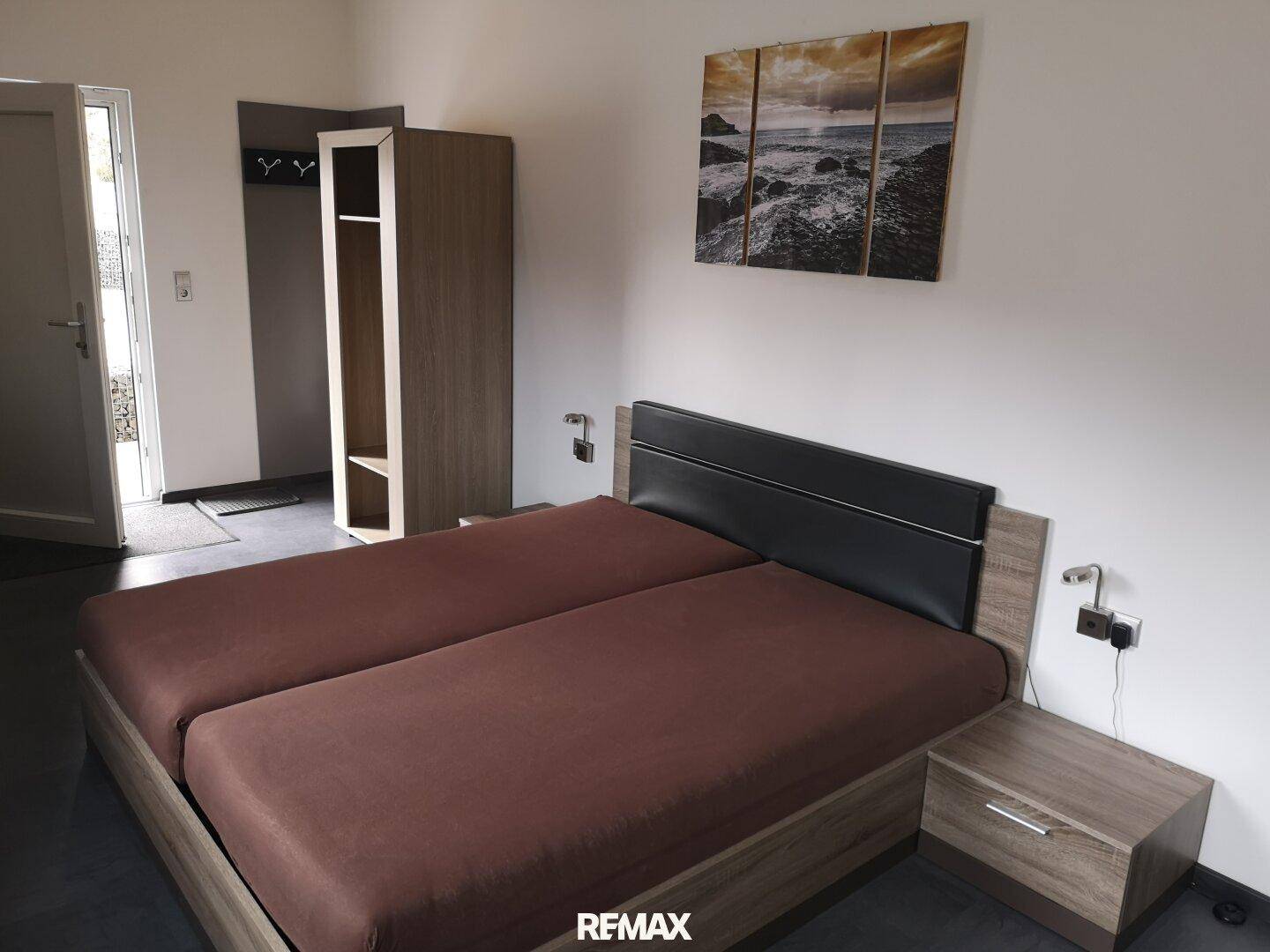 Schlafzimmer mit zwei Einzelbetten, Kleiderschrank und Nachttisch, mit Zugang nach draußen.