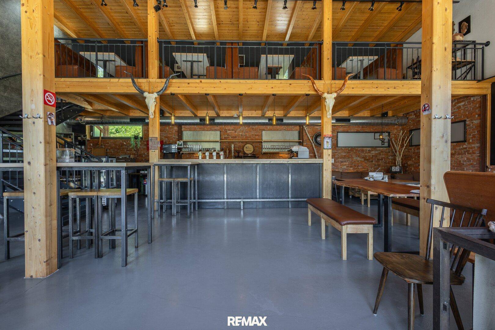 Geräumiger offener Gastraum mit Holzbalkendecke, Ziegelwänden und einer Bar im industriellen Stil.