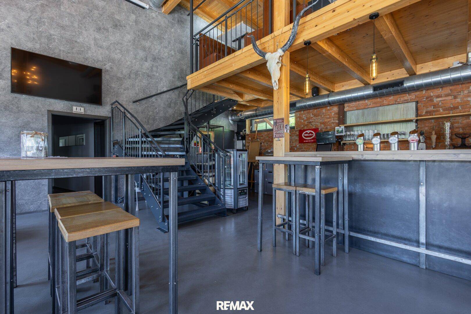 Bar- und Sitzbereich mit hohen Tischen, einer Wendeltreppe und industriellen Designelementen.