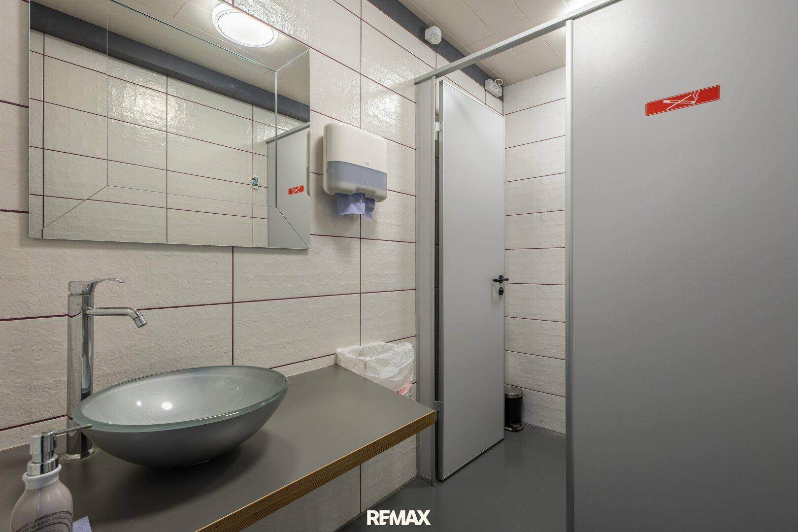Modern gefliestes WC mit Aufsatzwaschbecken und Spiegel.