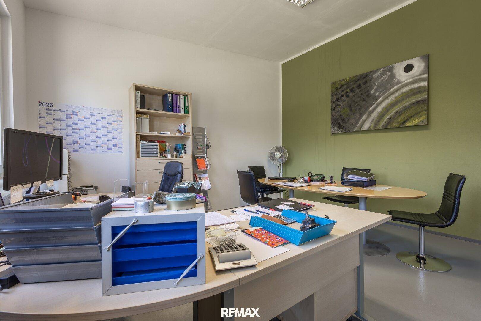 Geräumiges Büro mit Schreibtischen, Regalen und grüner Akzentwand.