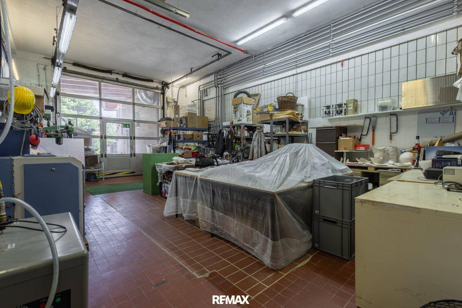 Geräumige Garage oder Werkstatt mit Fliesenboden und Rolltor, ideal für Lagerung oder Arbeiten.
