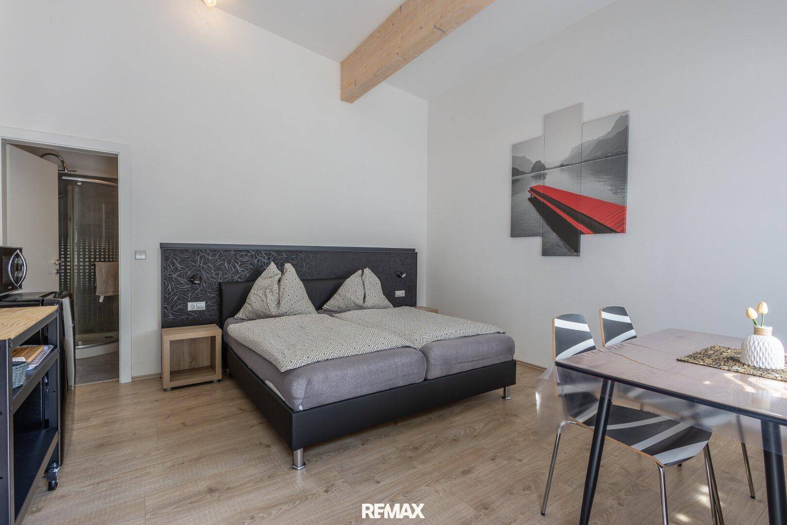 Helles Schlafzimmer mit Doppelbett, Esstisch und Holzbalken.