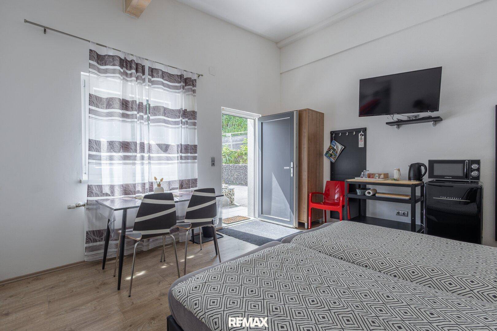 Helles Schlafzimmer mit zwei Einzelbetten, kleinem Essbereich und direktem Zugang zum Außenbereich.