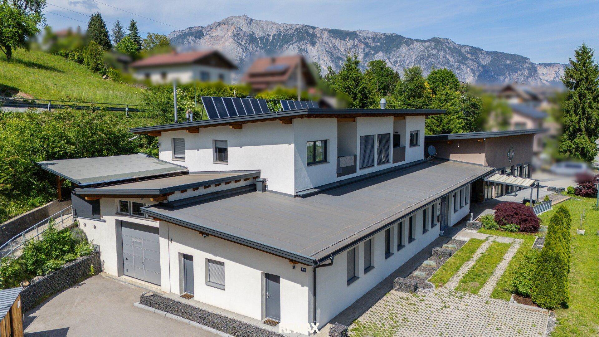 Modernes Gebäude mit Flachdach und Solarpaneelen vor einer beeindruckenden Bergkulisse.