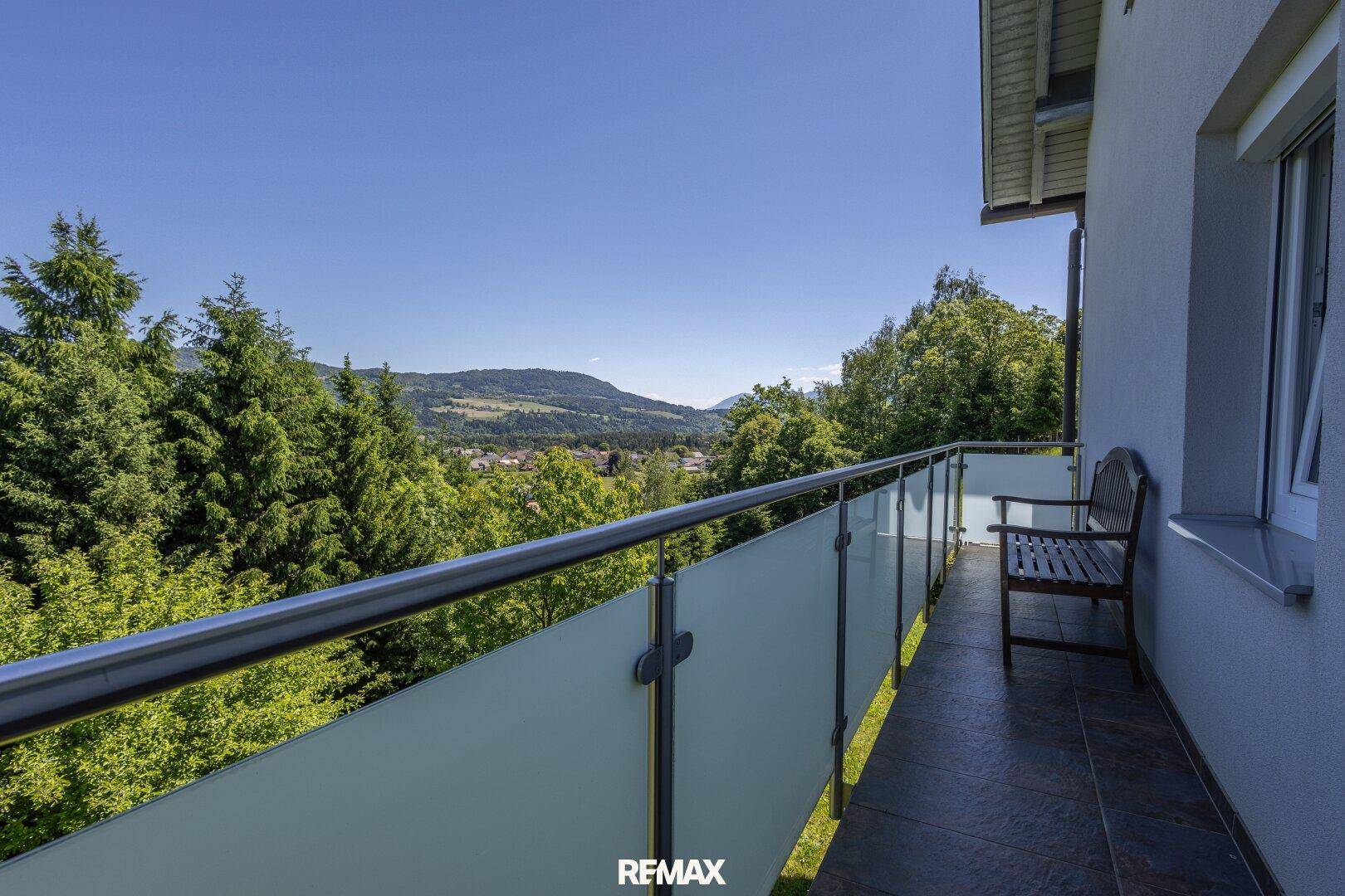 Balkon mit Glasbrüstung und weitem Blick über die grüne Landschaft und Berge.