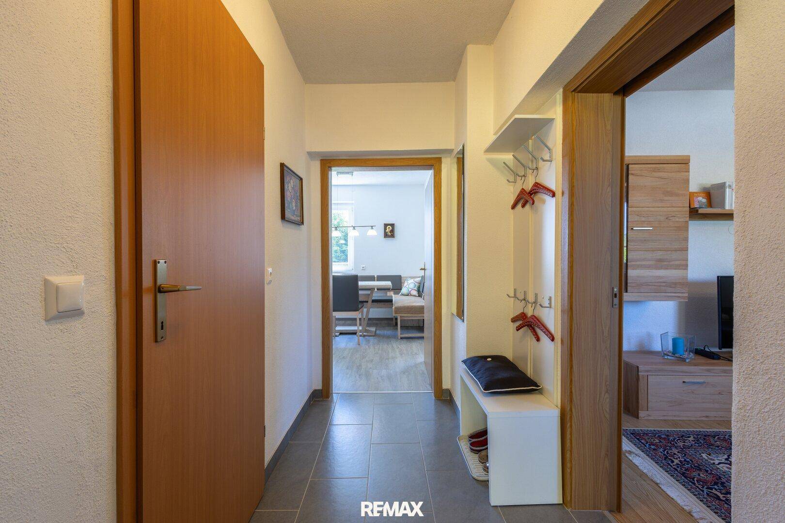 Heller Flur mit Fliesenboden und Garderobe, der zu verschiedenen Räumen führt.