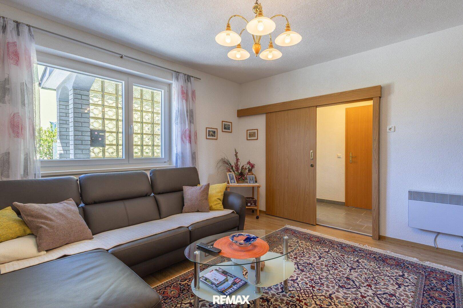 Helles Wohnzimmer mit bequemer Couch, Holzboden und Schiebetür zu einem weiteren Raum.