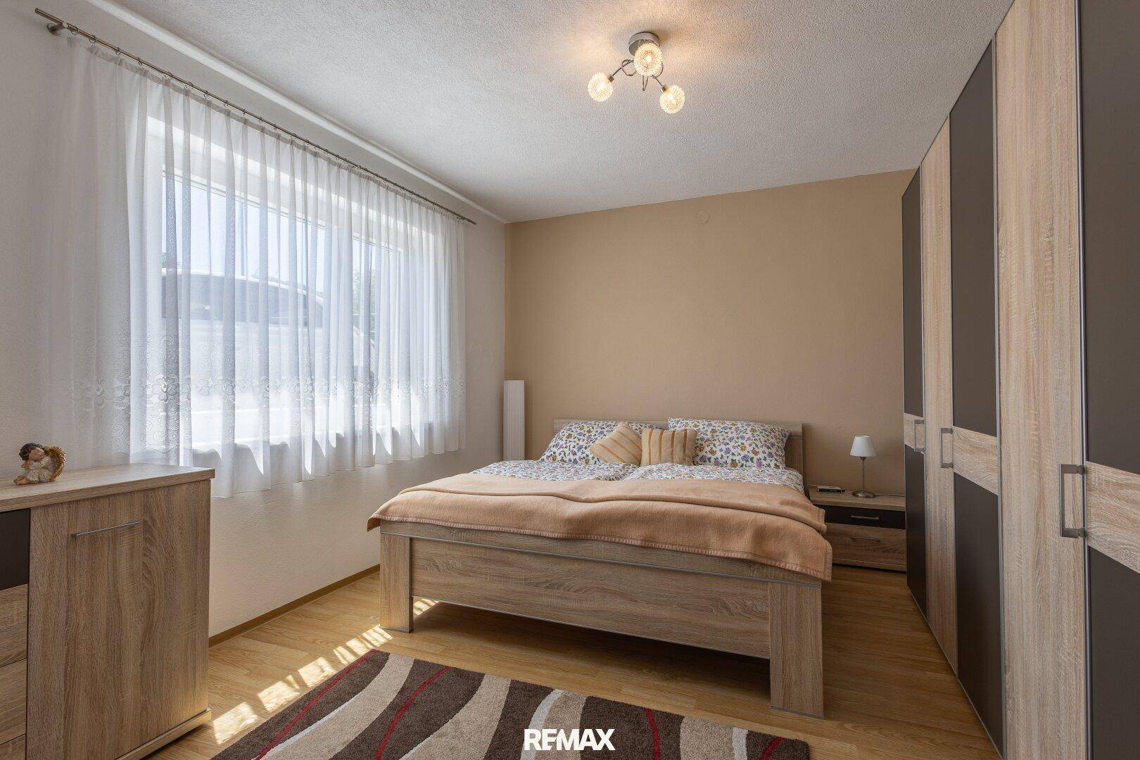 Schlafzimmer mit Doppelbett, Holzmöbeln und großem Fenster für viel Tageslicht.