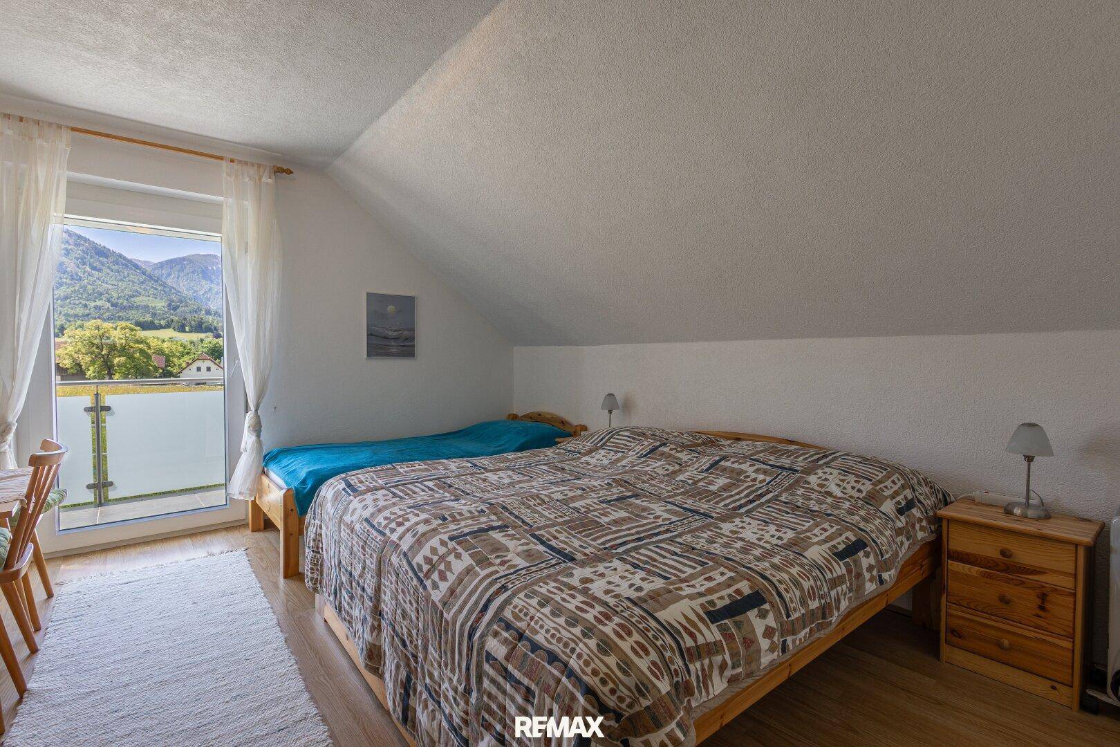 Schlafzimmer im Dachgeschoss mit Doppelbett, Holzboden und Balkonzugang.