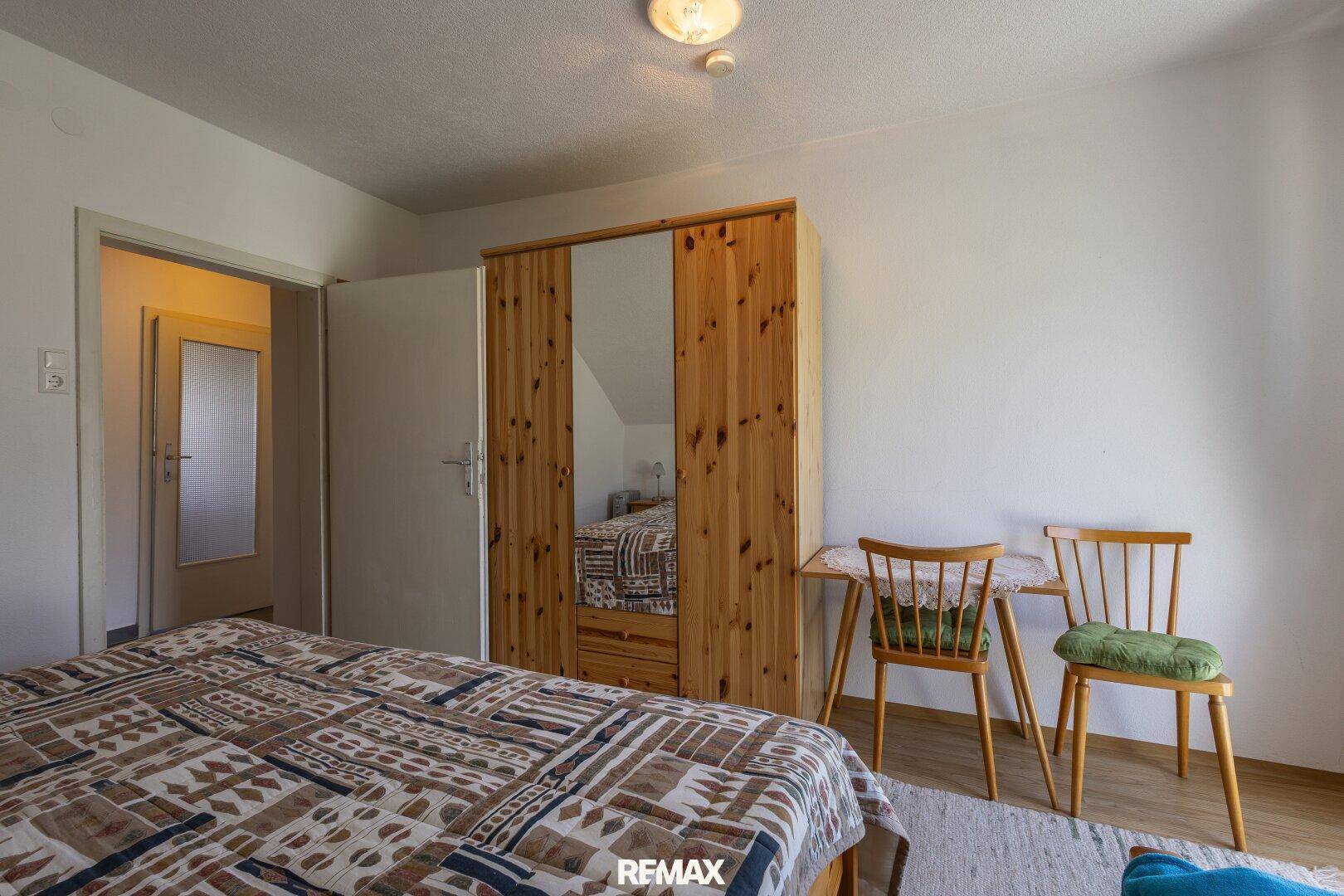 Gemütliches Schlafzimmer im Dachgeschoss mit Holzschrank und Zugang zu einem weiteren Raum.