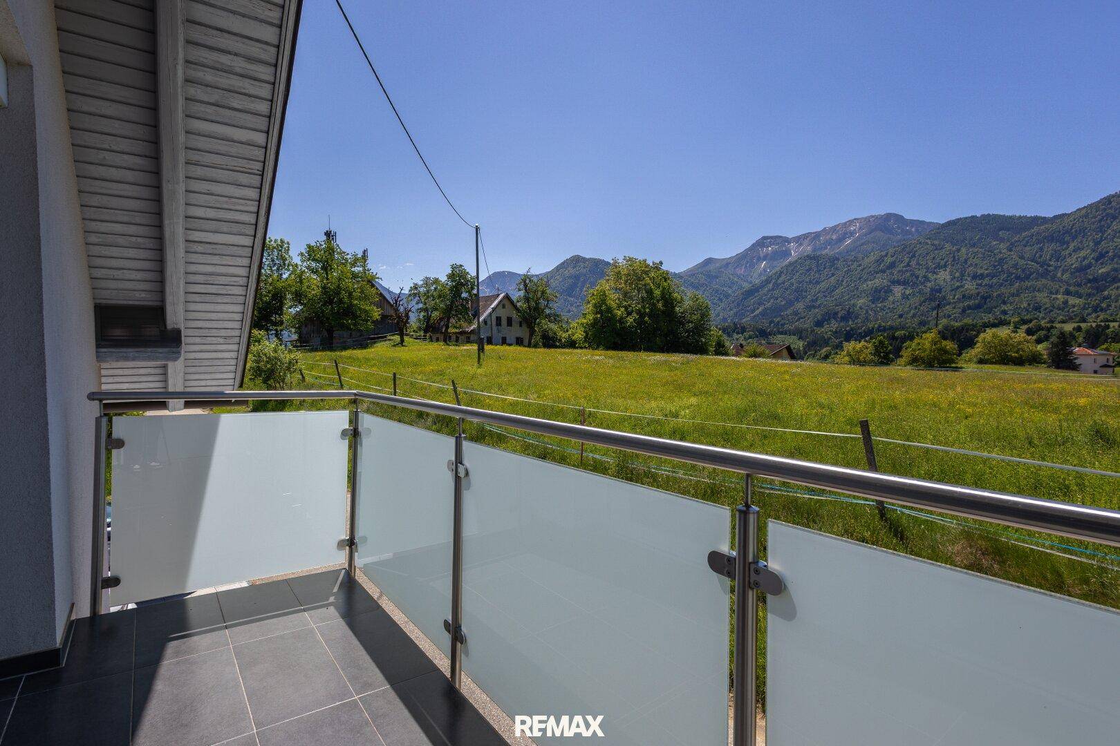 Balkon mit Glasbrüstung und weitem Blick über die grüne Landschaft und Berge.