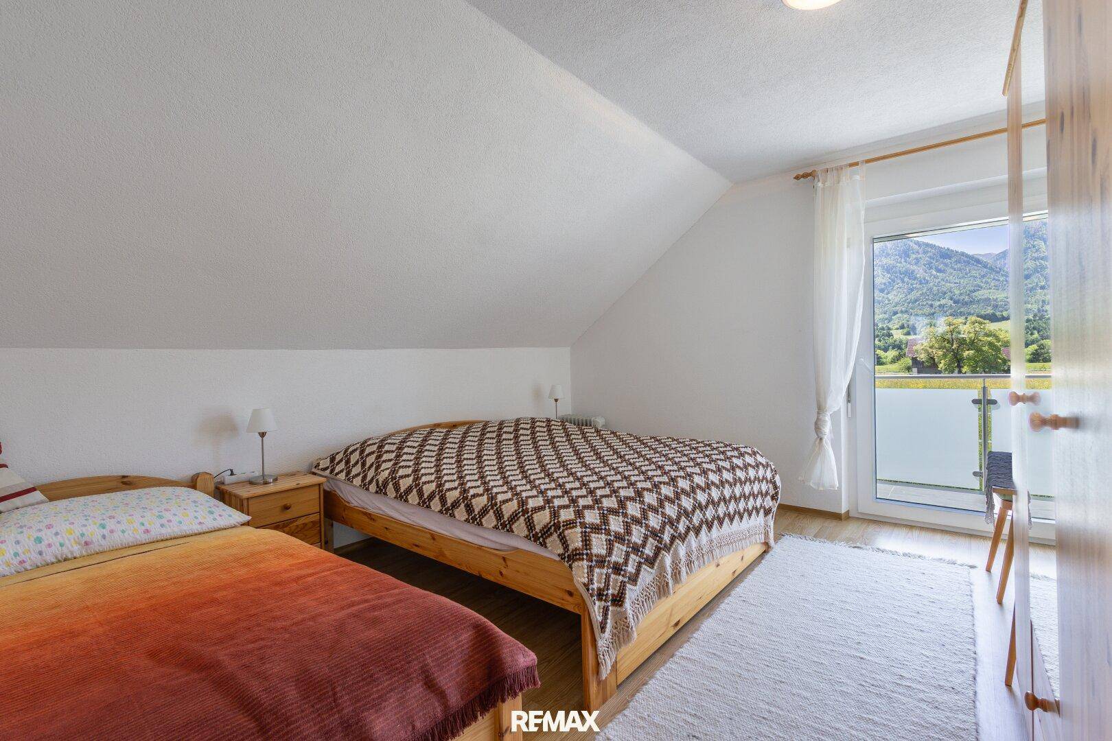 Helles Schlafzimmer im Dachgeschoss mit zwei Betten und Balkonzugang.