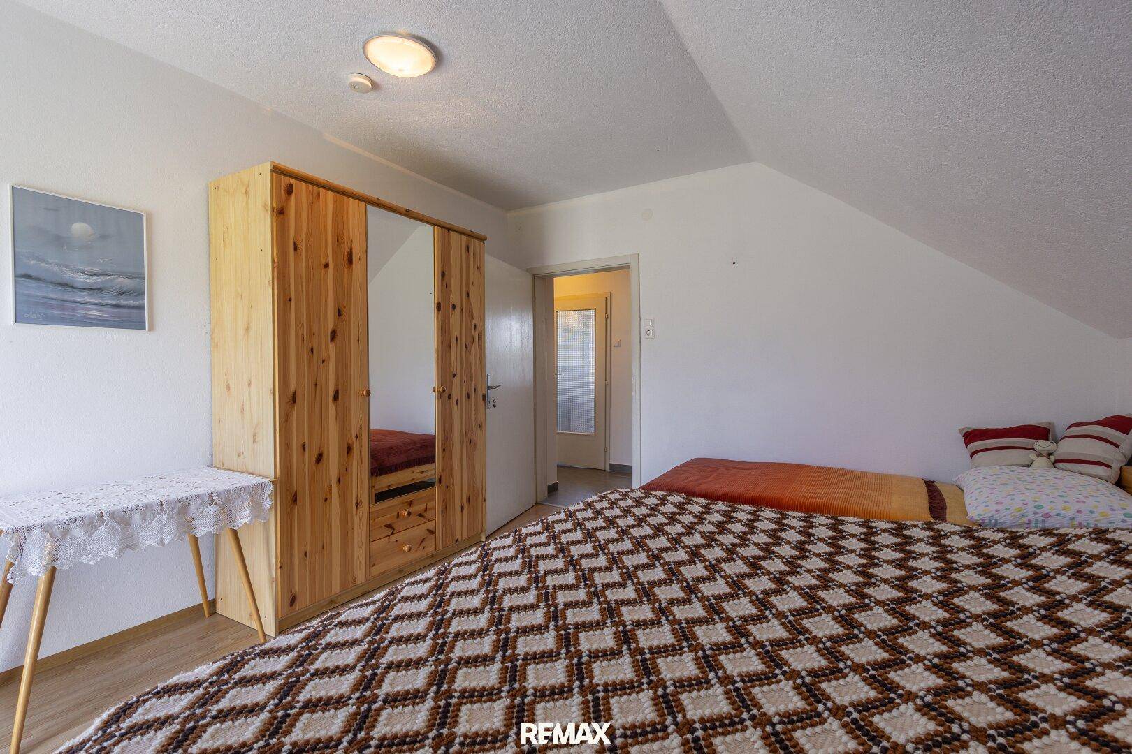 Schlafzimmer im Dachgeschoss mit Holzboden und Kleiderschrank, angrenzend an einen Flur.
