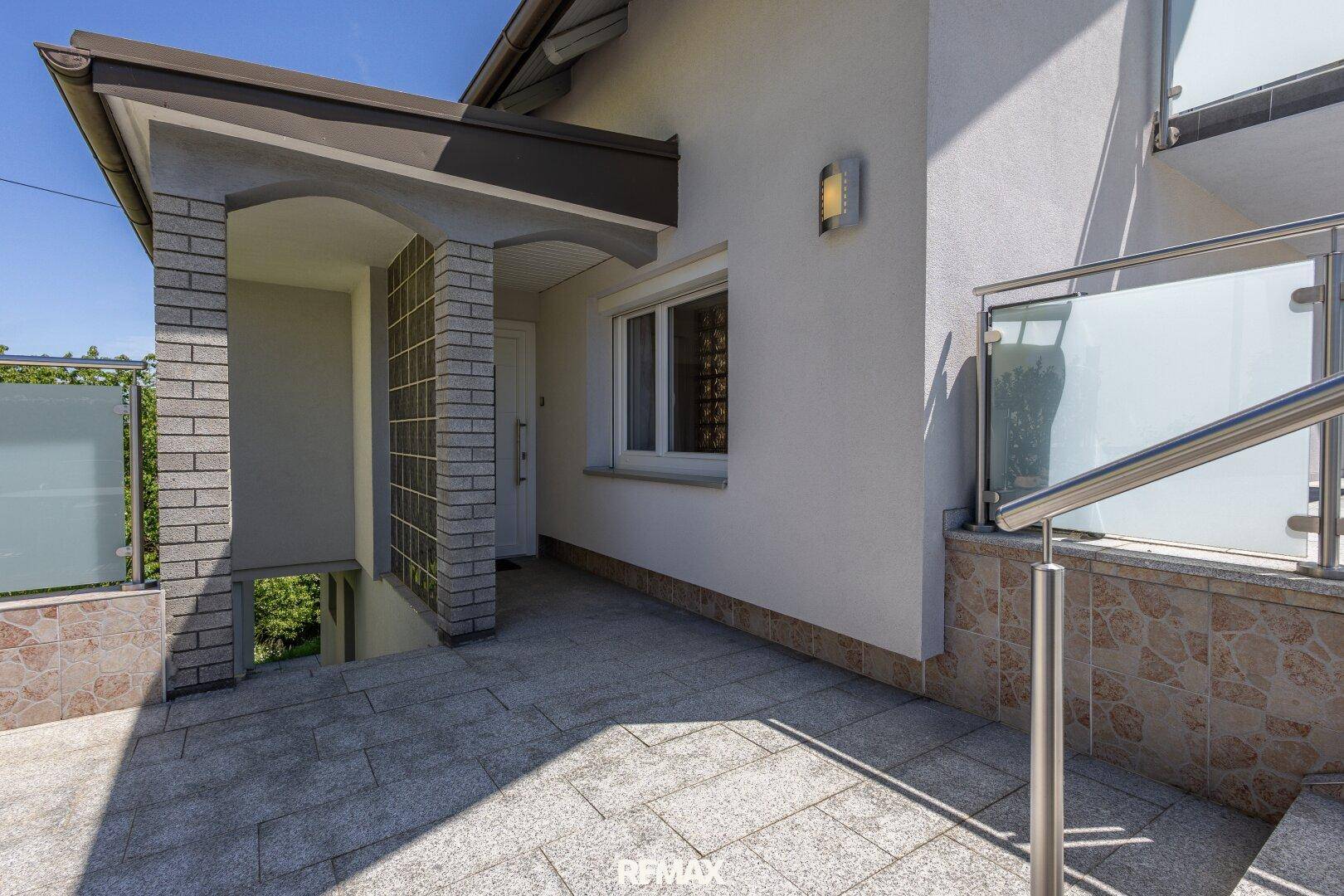 Eingangsbereich des Hauses mit Steintreppe und moderner Glasbrüstung.