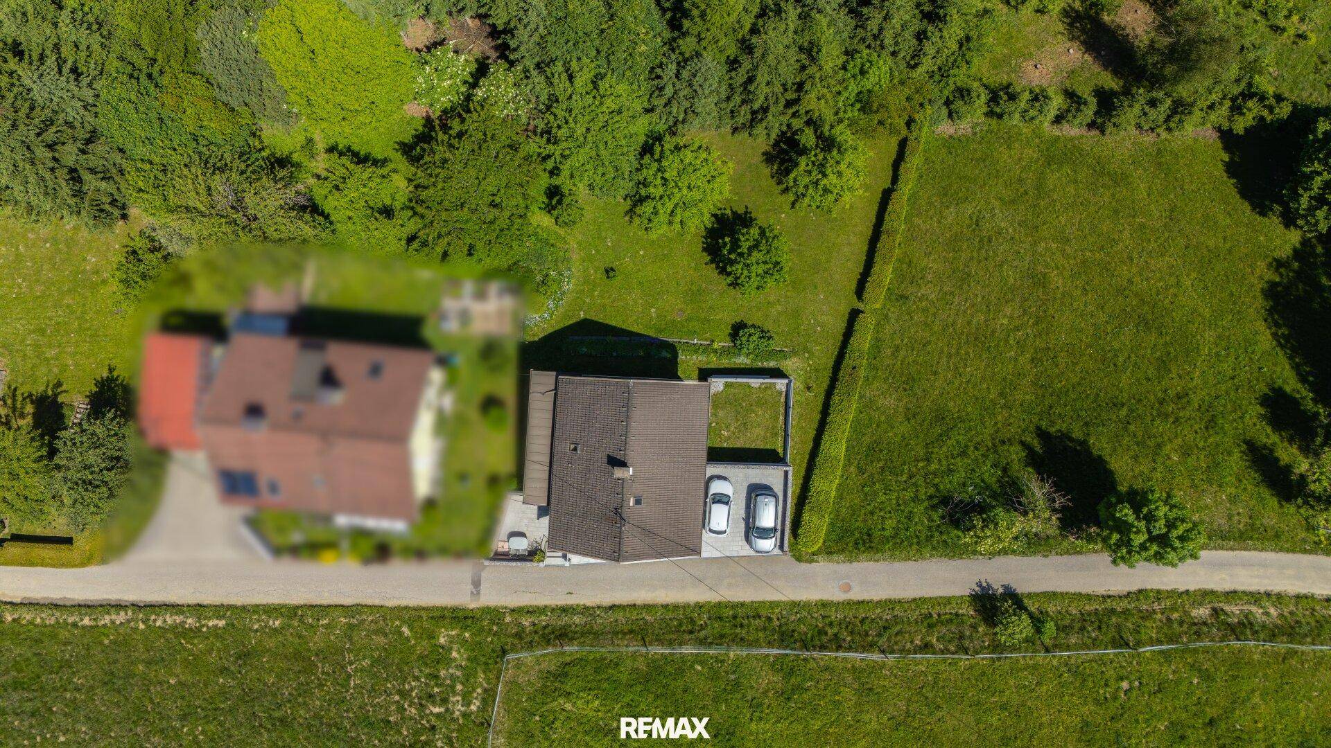 Draufsicht des Grundstücks mit Haus, Garten und zwei geparkten Autos auf der Einfahrt.