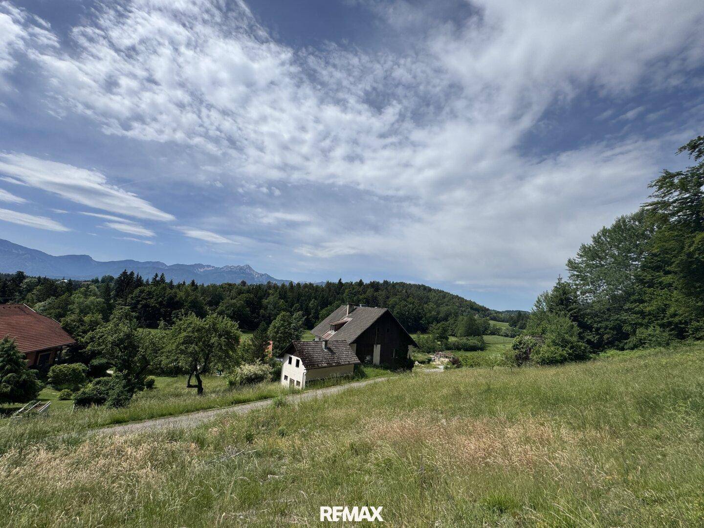 Sanfter grüner Hang mit einem traditionellen Haus und weitem Blick auf die Bergkette.