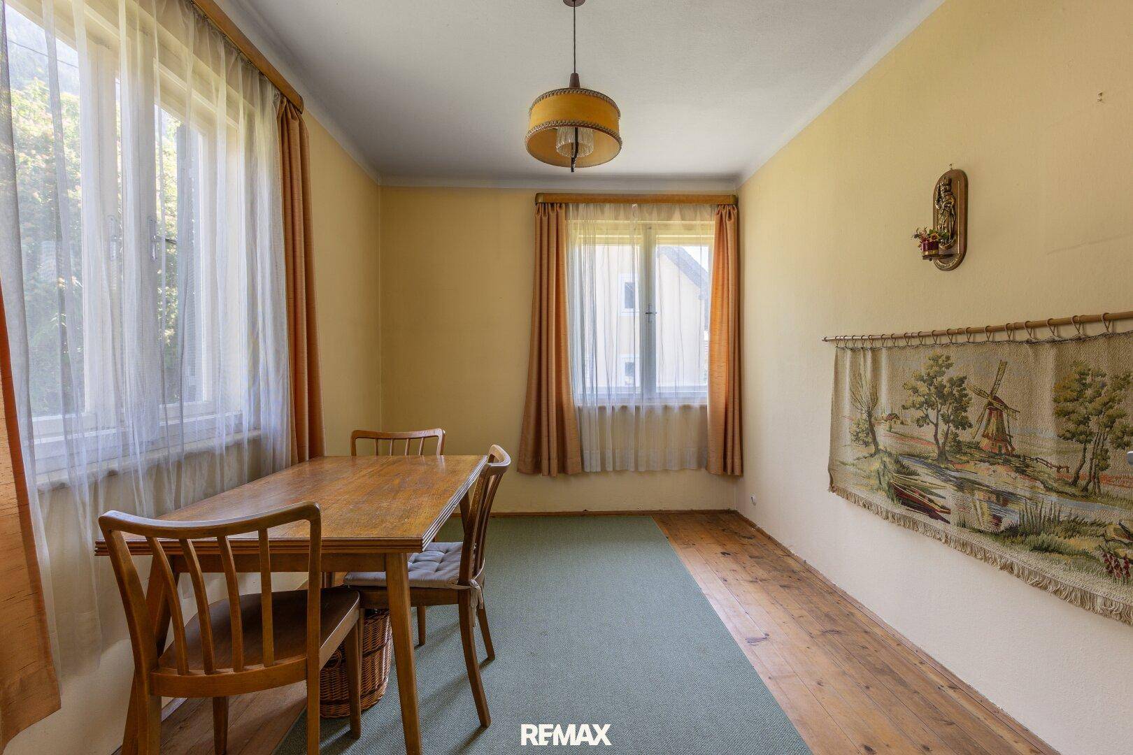 Esszimmer mit Holztisch, Stühlen und Teppichboden, umgeben von Fenstern für natürliches Licht.