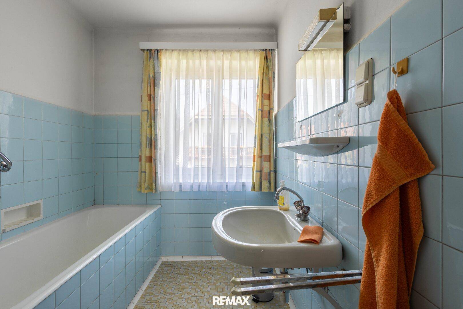 Badezimmer mit hellblauen Fliesen, Badewanne, Waschbecken und Fenster.