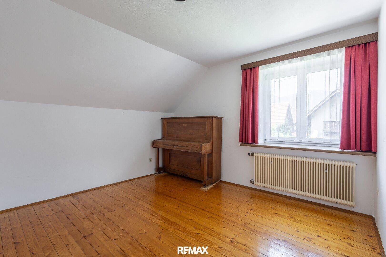 Schlafzimmer im Dachgeschoss mit Holzboden, Fenster und einem Klavier.