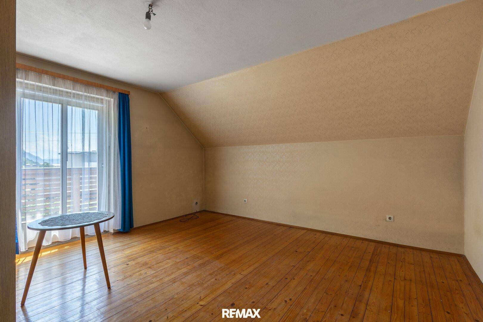Schlafzimmer im Dachgeschoss mit Holzboden, Fenster und Blick auf die Umgebung.